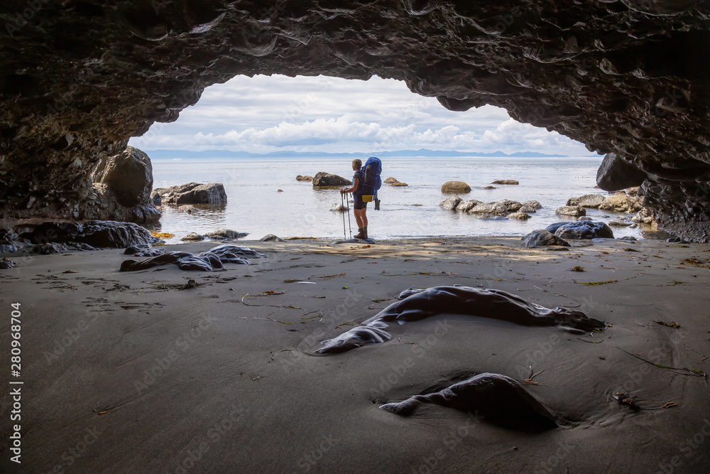 Adventurous girl hiking in a cave on Juan de Fuca Trail to Mystic Beach on the Pacific Ocean Coast d