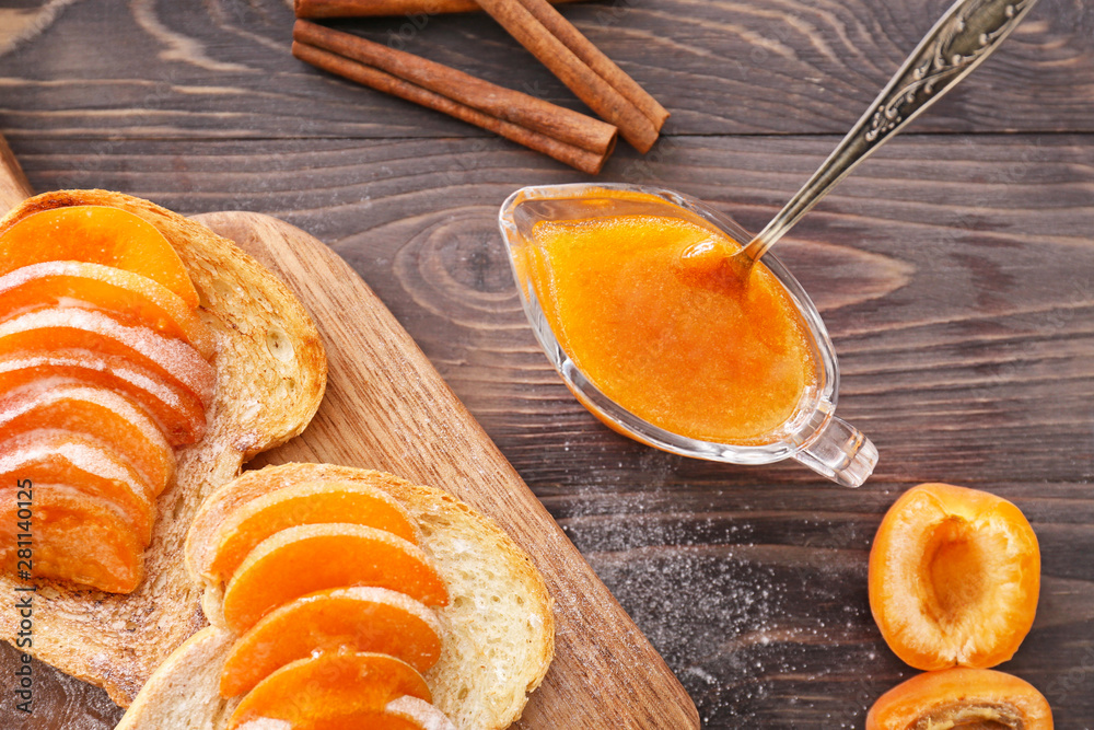 Bread slices with tasty apricot jam on wooden table