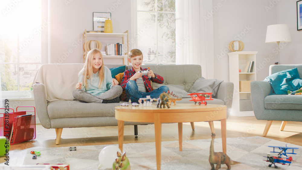 在家：聪明的男孩在电子游戏控制台里玩，使用操纵杆控制器，他的姐姐坐在N