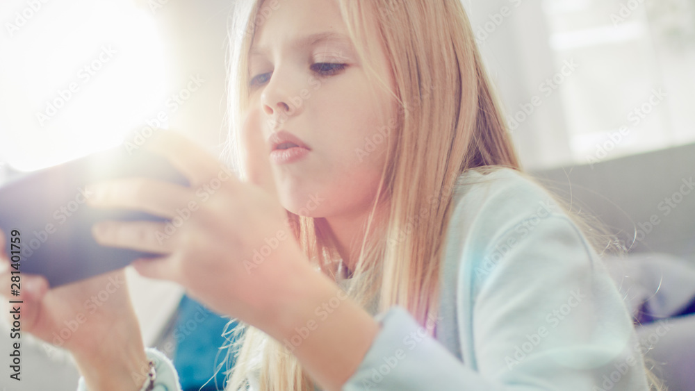 一个聪明女孩坐在家里地毯上用智能手机玩电子游戏的特写肖像，