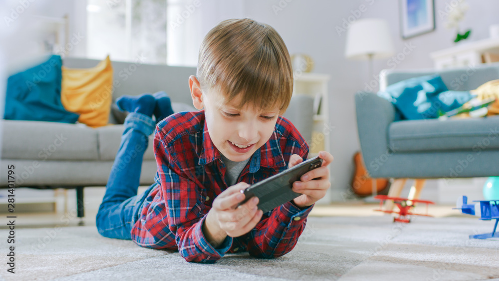 躺在地毯上的聪明小男孩用智能手机玩电子游戏，手里拿着手机
