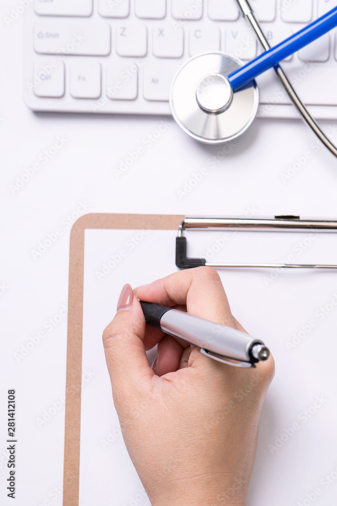女医生用听诊器在白色工作台上的剪贴板上写病历。