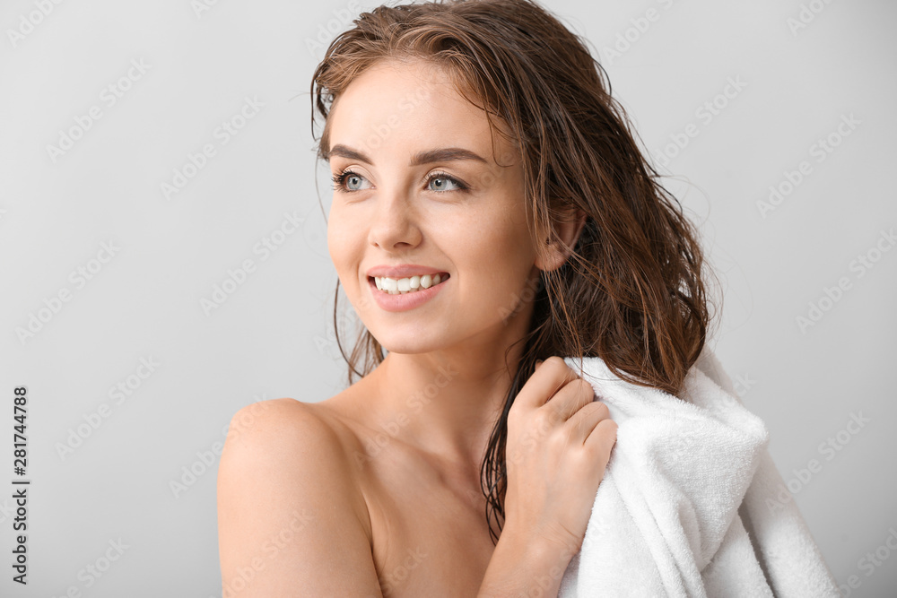 美丽的年轻女子在灰色背景下洗完头发后擦拭头发