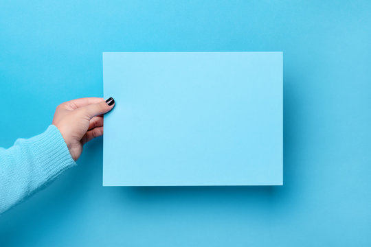 piece of paper in the female hand over blue trendy background, empty blank for advertisement