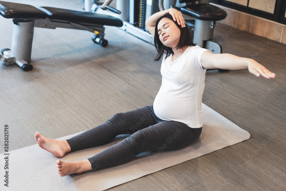 活跃的孕妇在瑜伽室的健身中心锻炼。年轻的孕妇抱着ba