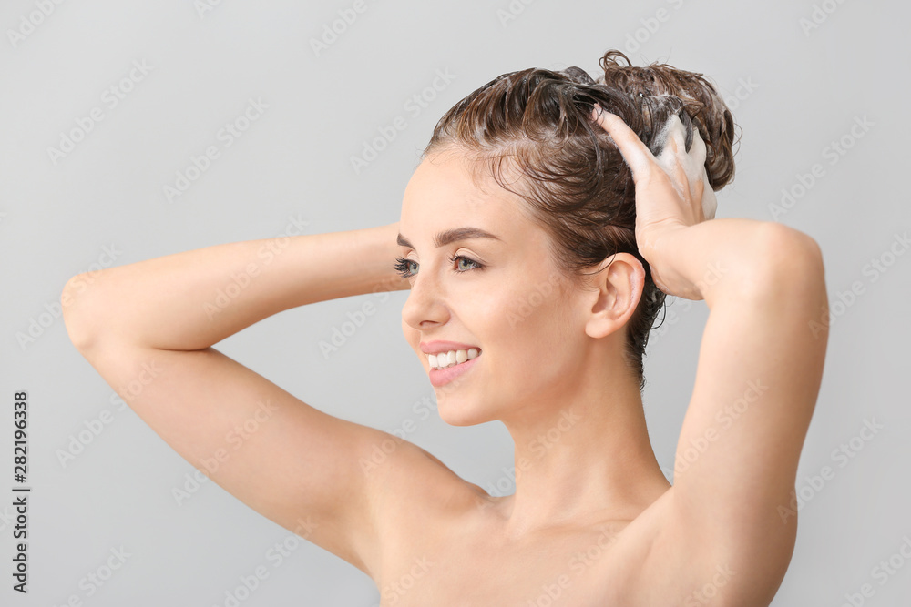 美丽的年轻女子在灰色背景下洗头