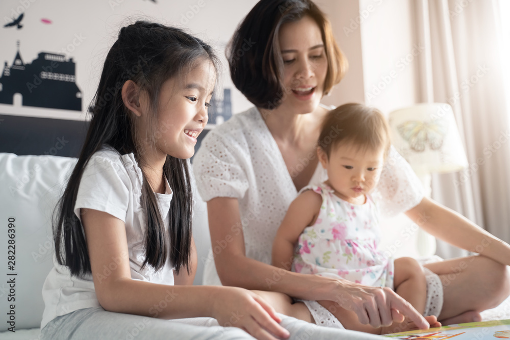 家庭快乐活动。亚洲美女坐在沙发上给女儿读音乐书