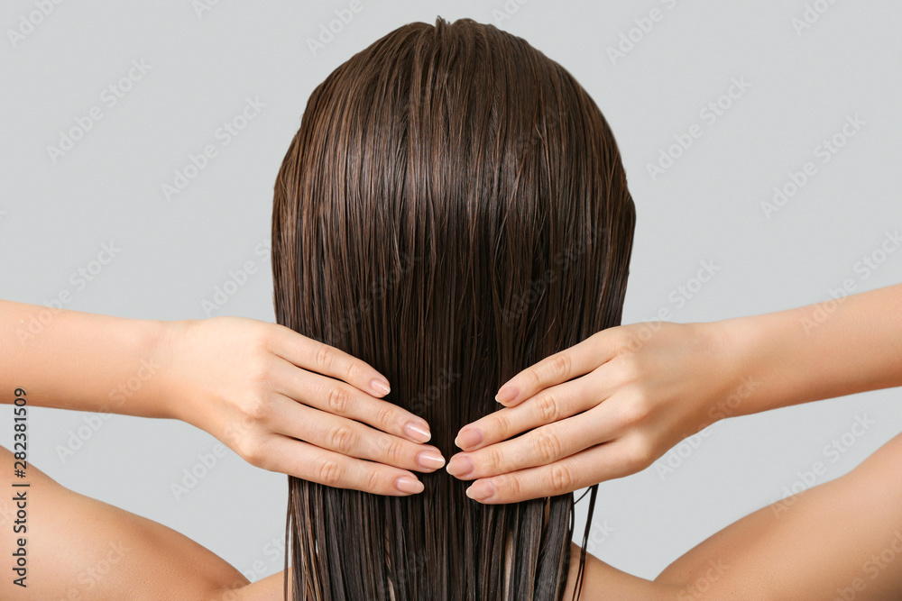 Beautiful young woman after washing hair against grey background, back view