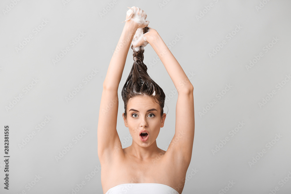 有趣的年轻女子在灰色背景下洗头