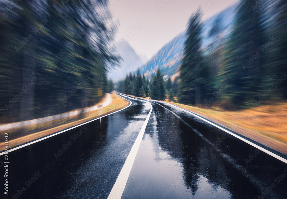 Road in the autumn forest in rain with motion blur effect. Perfect asphalt mountain road in overcast