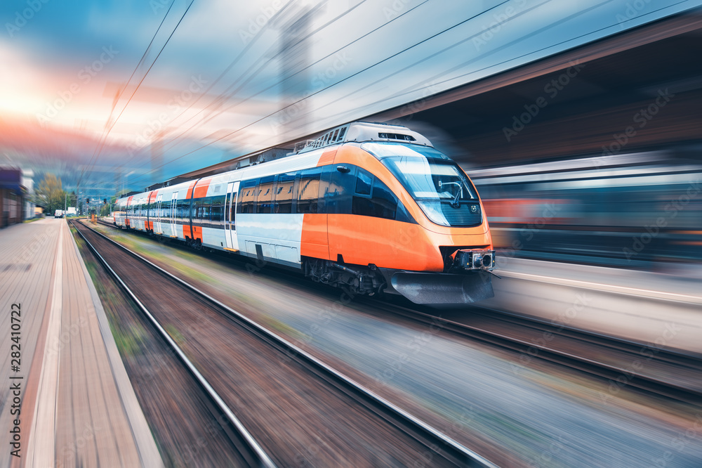 日落时分，高速橙色列车在火车站上行驶。现代城际客运列车