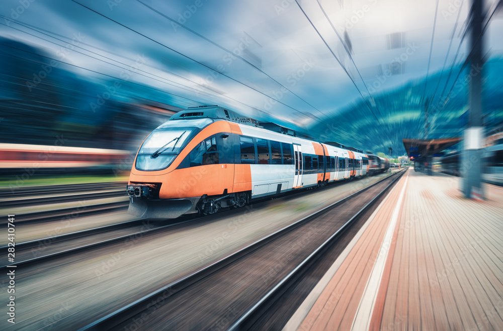 High speed orange train in motion on the railway station at sunset. Modern intercity passenger train