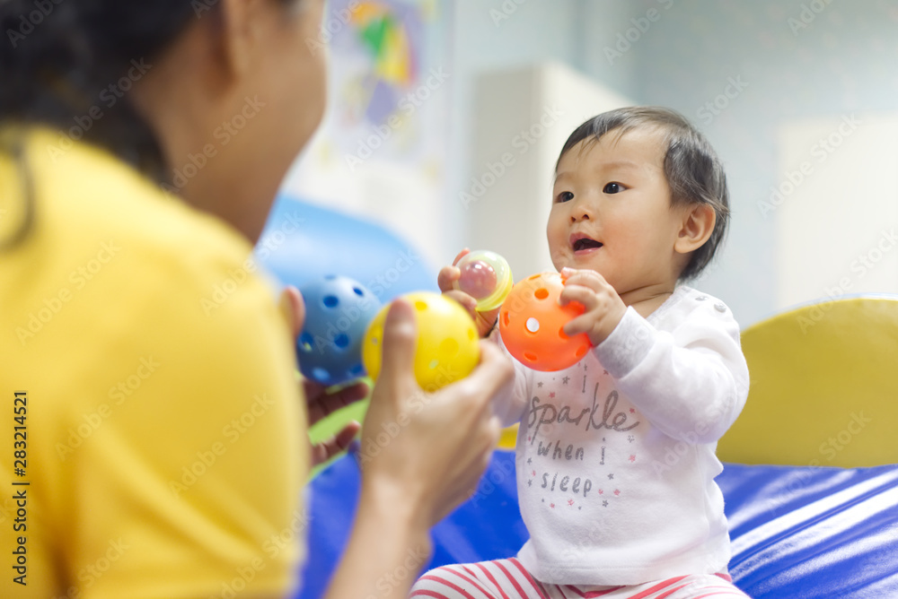 年轻的亚洲小婴儿在教室里拿着球和玩具与女幼师玩耍。K