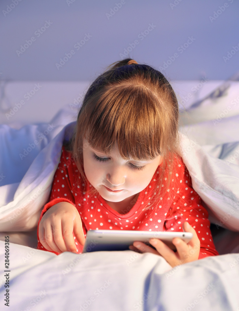 可爱的小女孩晚上在床上使用平板电脑