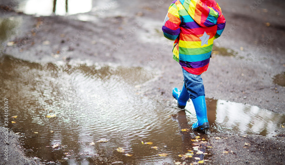 雨天孩子穿着雨鞋在水坑里行走