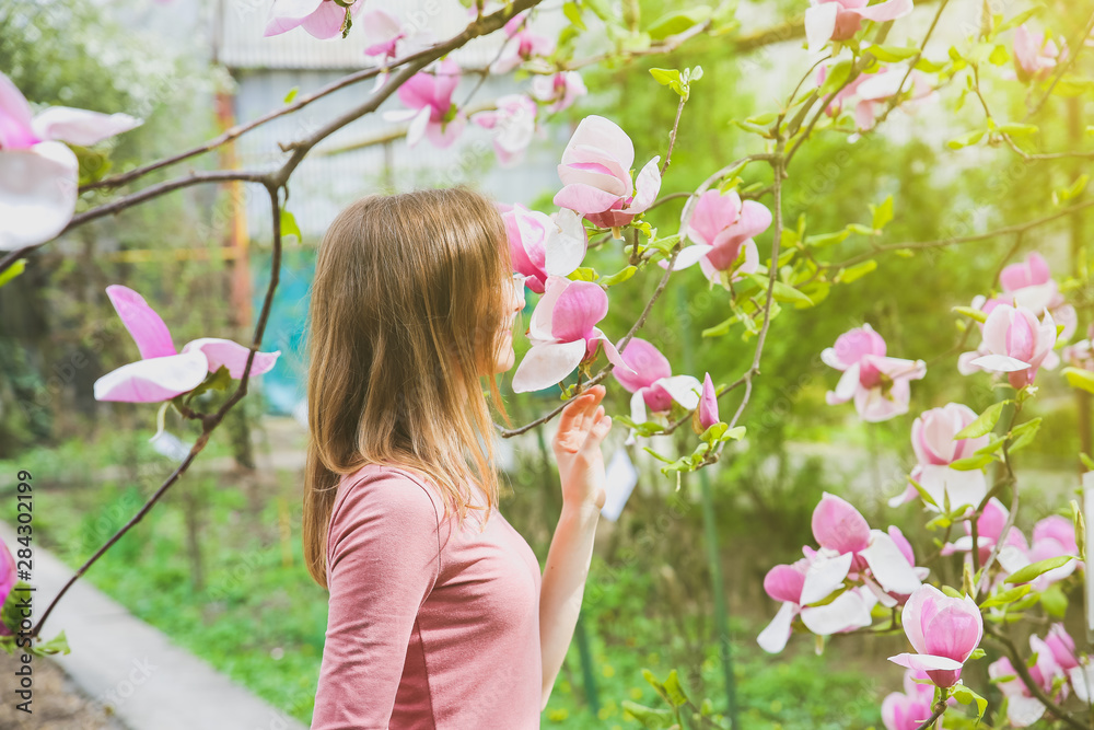Beautiful girl near blooming tree. Blossom magnolia outdoors.  Spring mood. Woman relaxing.