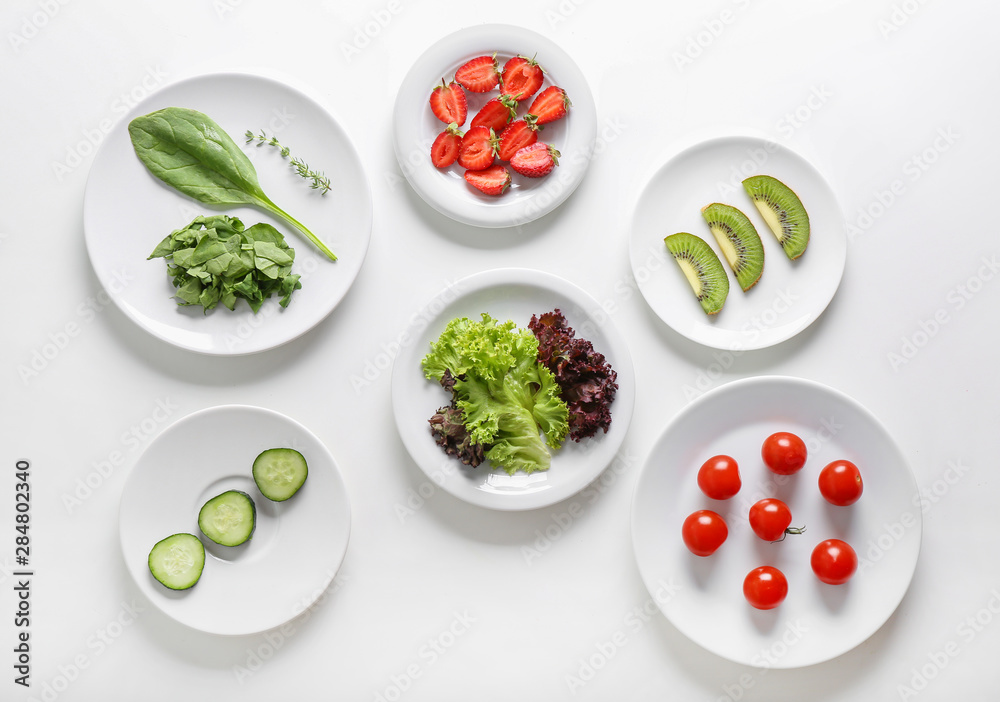 Plates with lettuce, vegetables, kiwi, strawberry and herbs on white background