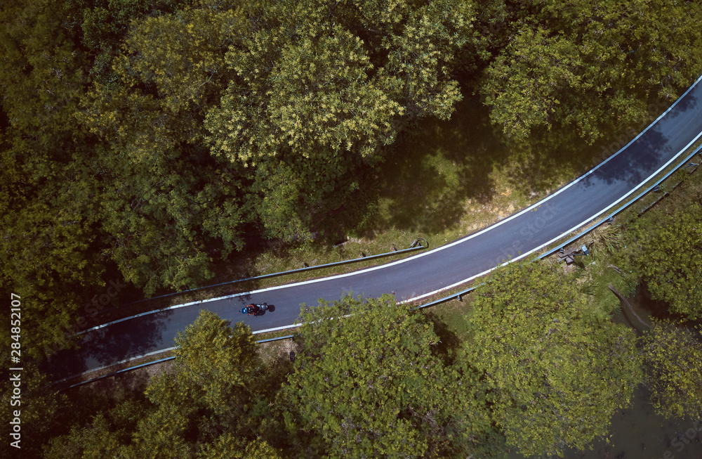 马来西亚乡村公路摩托车骑手森林鸟瞰图。