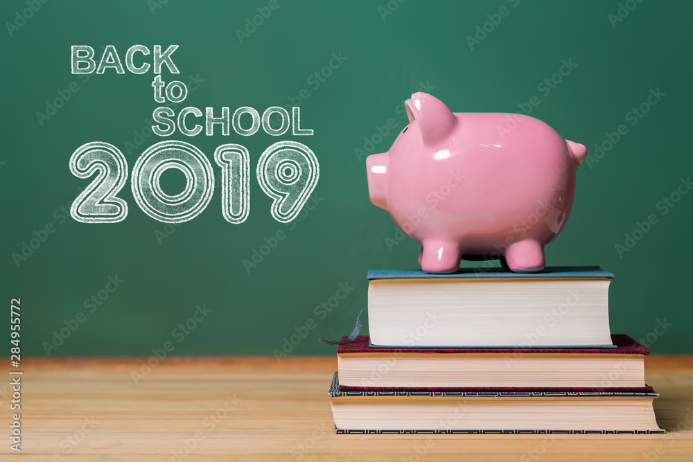 Back to School 2019 text with pink piggy bank on top of books with chalkboard