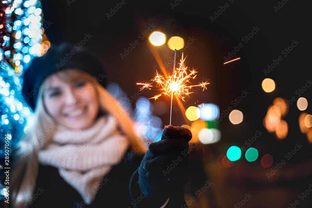 圣诞节或新年期间，快乐微笑的女孩站在明亮的城市街道上，手里拿着闪闪发光的东西