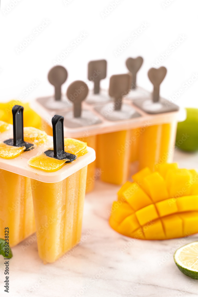 Fresh mango fruit popsicle ice in the plastic shaping box on bright marble table. Summer mood concep