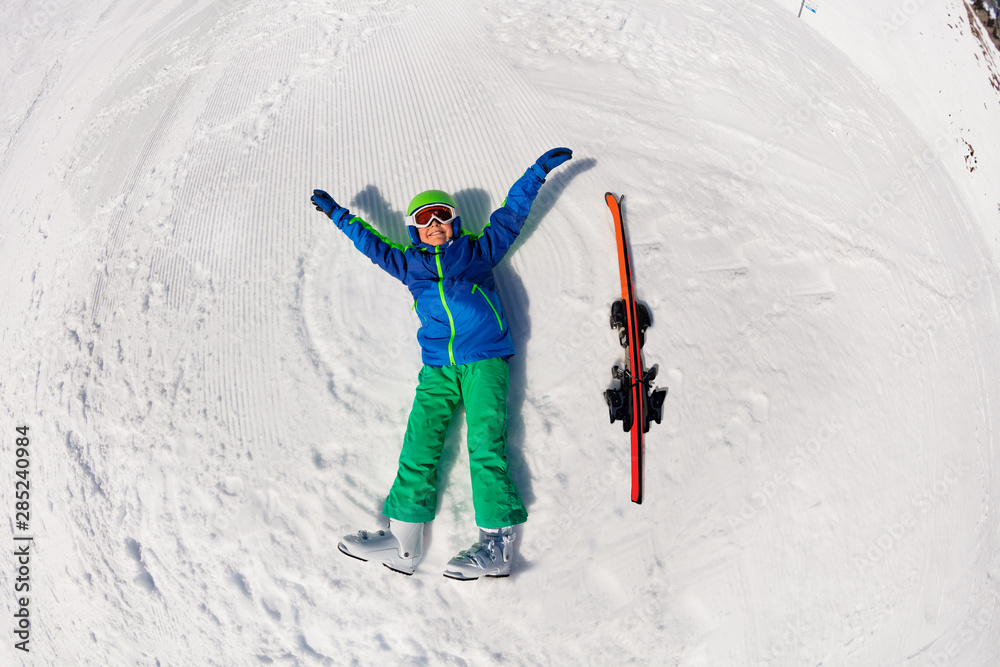 小男孩双手挥舞着滑雪板躺在雪坡上