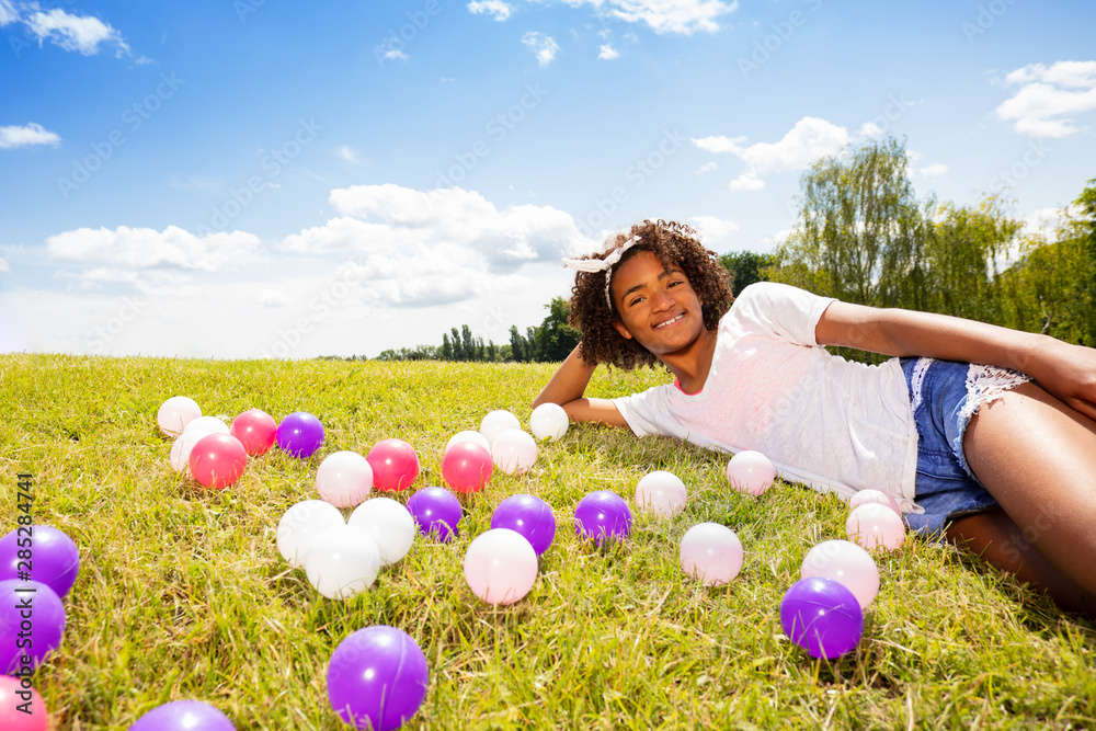 可爱的女孩躺在草地上，手里拿着五颜六色的球
