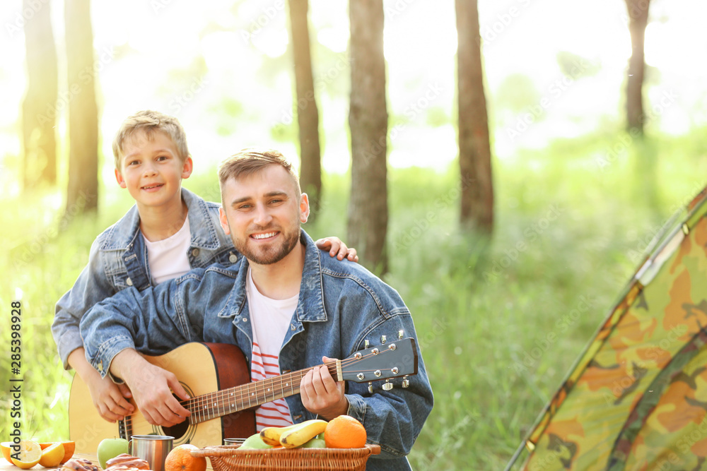 父亲和他的小儿子拿着吉他在森林里野餐