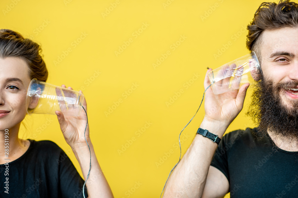 男人和女人用黄色背景上杯子做成的串电话交谈。沟通的概念