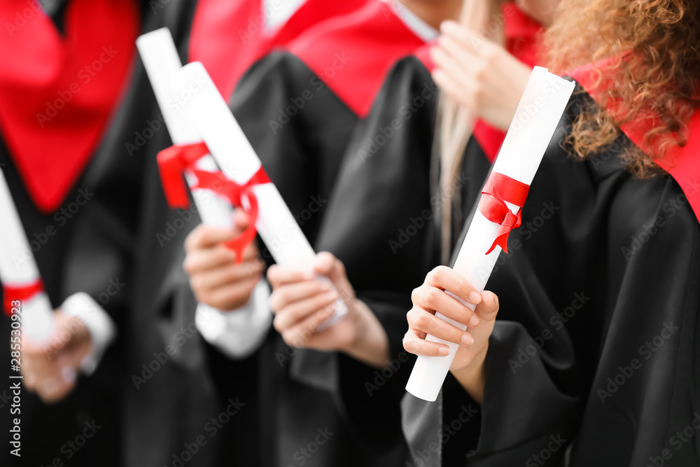 穿着学士长袍、拿着文凭的年轻学生在户外
