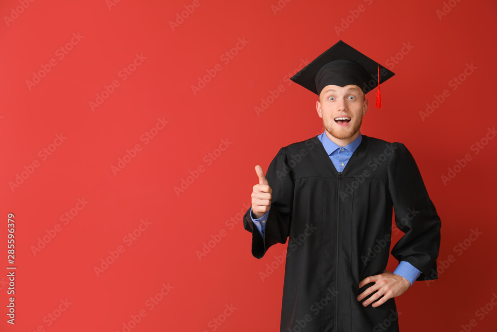 穿着学士袍的年轻男学生在彩色背景上竖起大拇指