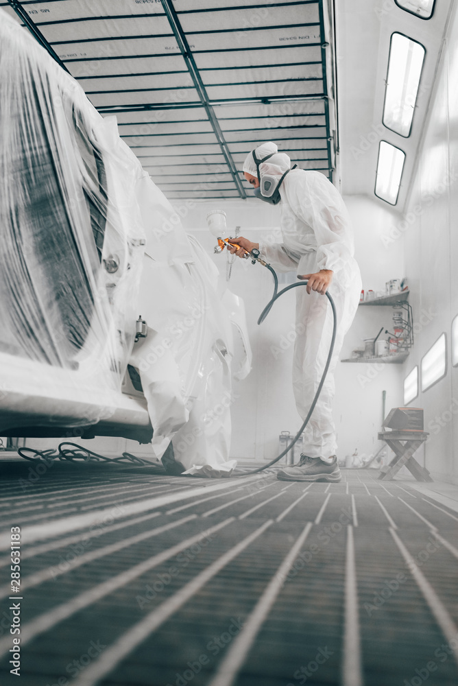 Worker painting car in a paint booth, low angle image.