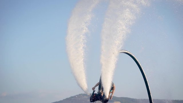 Flyboarding is a new extreme water sport. Athletic man performs tricks in flight. Spectacular sports coups and turns.