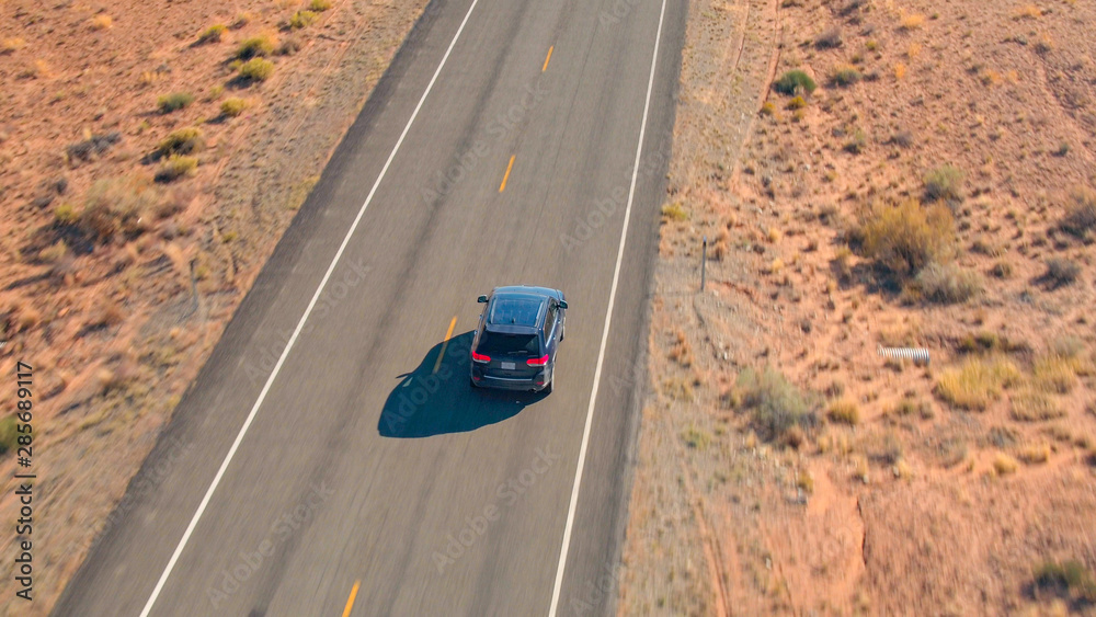 空中特写飞行在沙漠中空旷道路上行驶的黑色SUV汽车上方