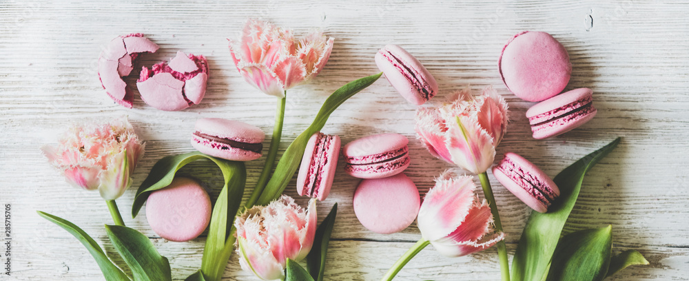 白色木质背景上，平放着甜粉色的马卡龙饼干和新鲜的春天郁金香花。