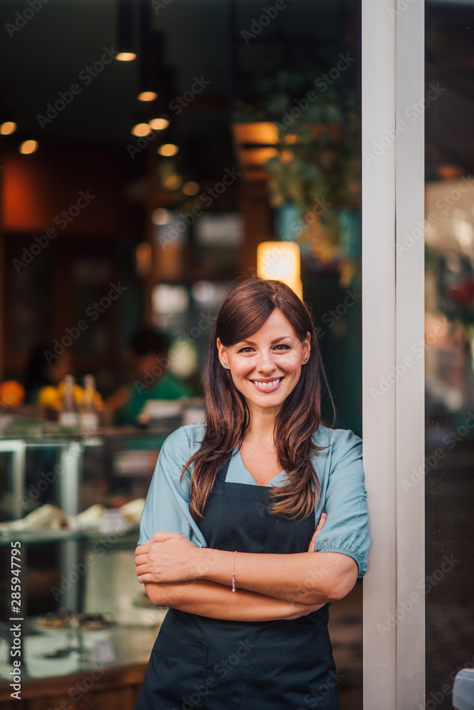 一位咖啡馆老板站在门口，对着镜头微笑的肖像。
