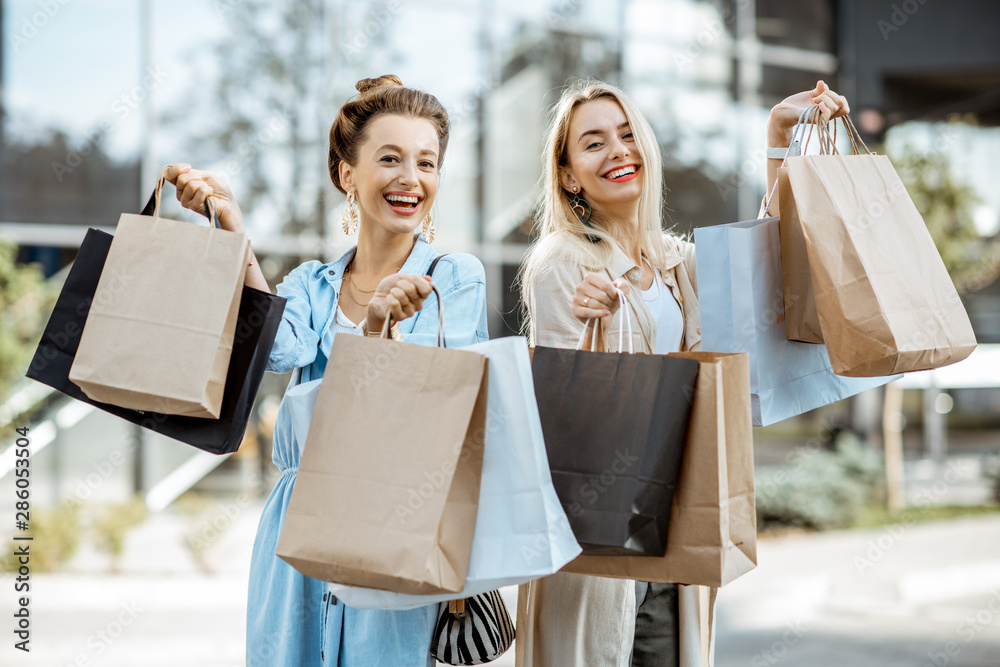 两个快乐的女朋友对购物感到兴奋，站在一起，前面放着购物袋