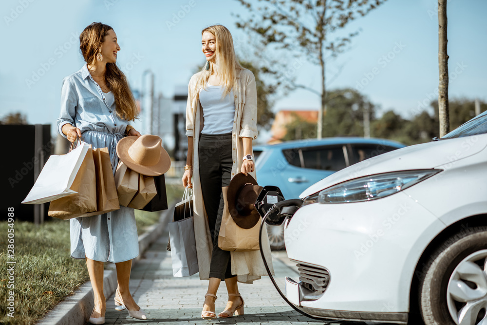 购物中心停车场上，妇女拿着购物袋走向电动汽车