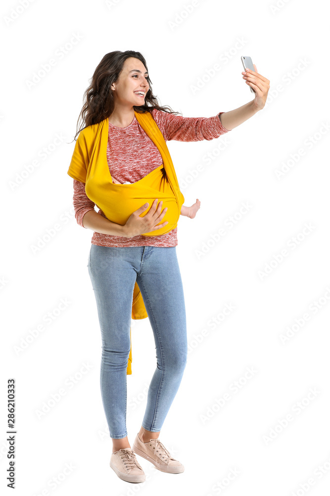 年轻的母亲带着穿着吊带的小婴儿在白底自拍