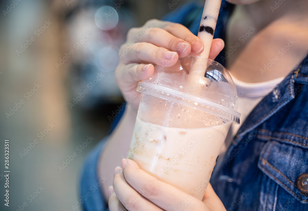 穿着牛仔夹克的年轻女孩正在用杯子喝红糖口味的木薯珍珠泡奶茶