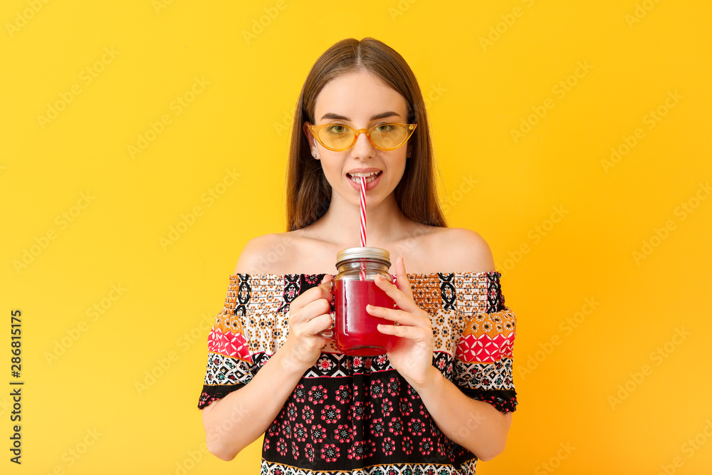 Young woman drinking healthy juice on color background