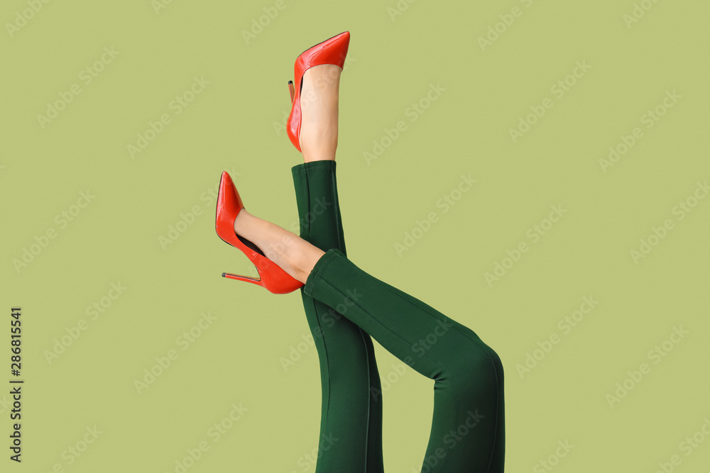 Legs of young woman in high-heeled shoes and pants on color background