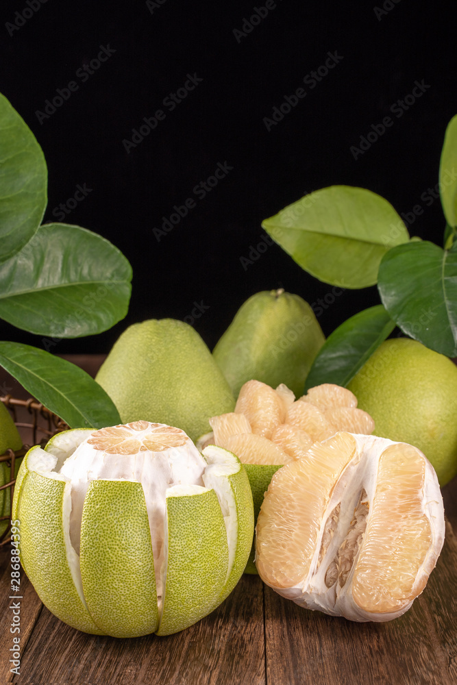 新鲜去皮的柚子、葡萄柚、柚子和绿叶柚子放在深色木板桌上。时令水果