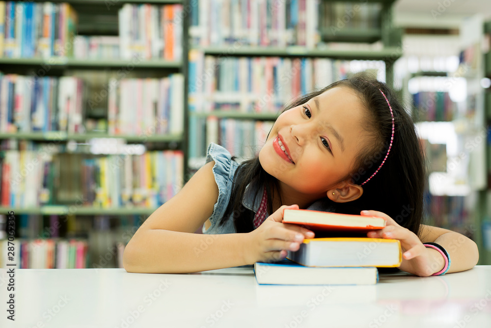 微笑可爱的亚洲小女孩坐在学校图书馆里，抬头思考未来，教育