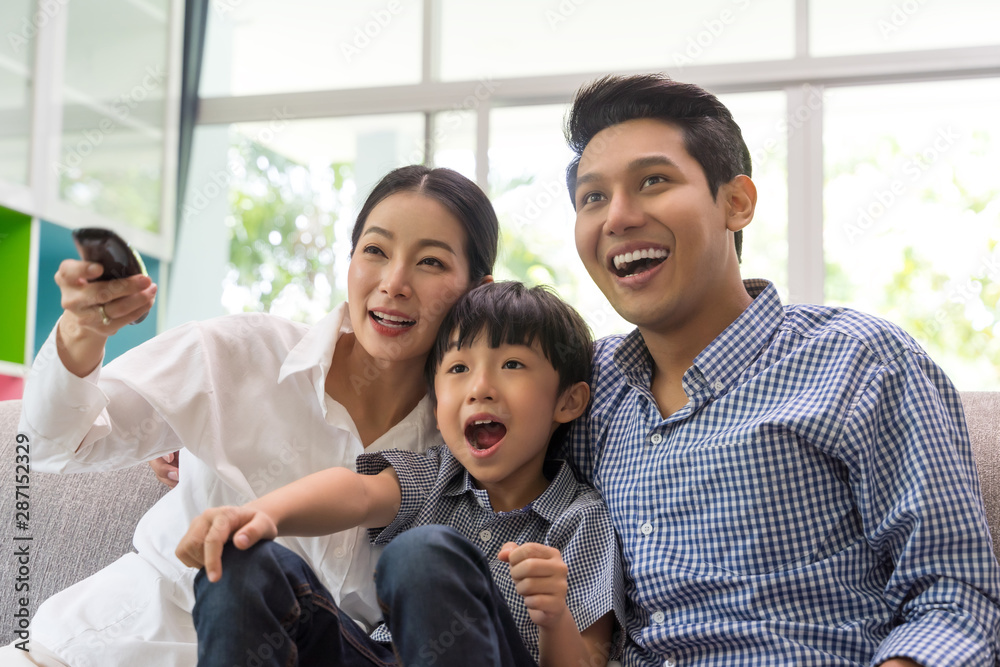 幸福的亚洲家庭在客厅的沙发上一起看电视。家庭和家的概念