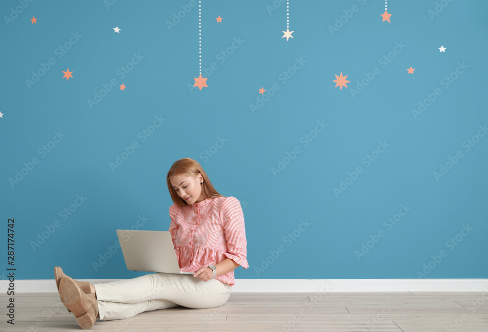 年轻的女博主拿着笔记本电脑坐在彩色墙上