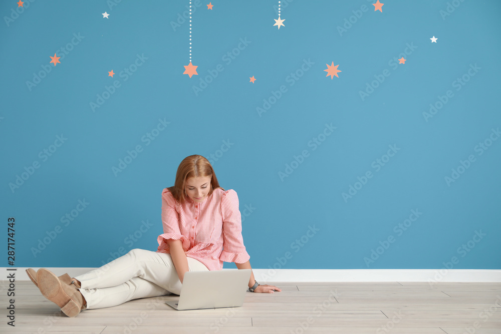 年轻的女博主拿着笔记本电脑坐在彩色墙上
