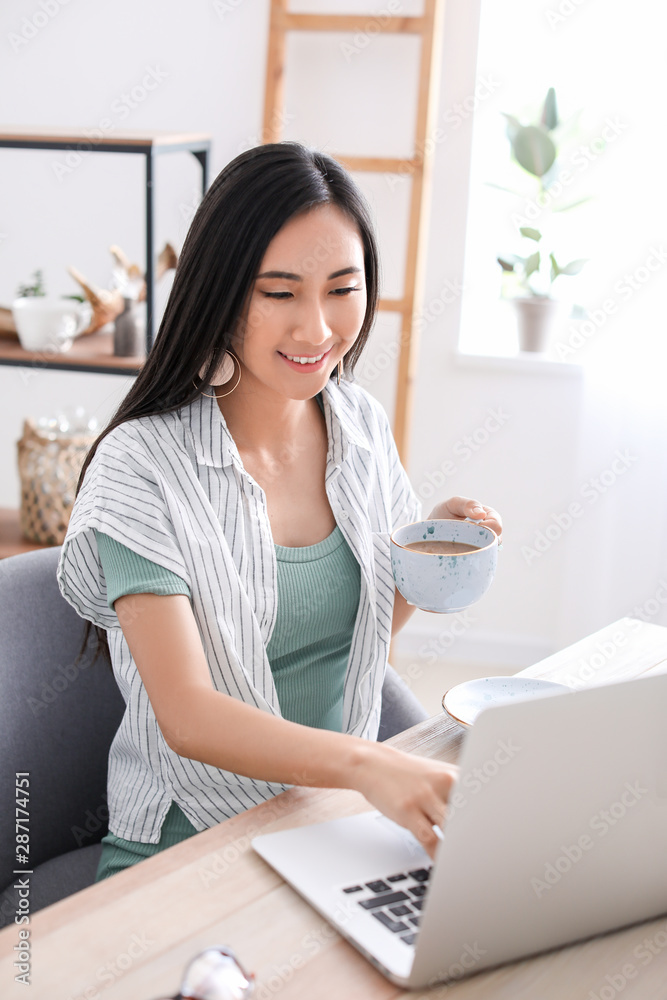 坐在桌上用笔记本电脑喝咖啡的亚洲博主