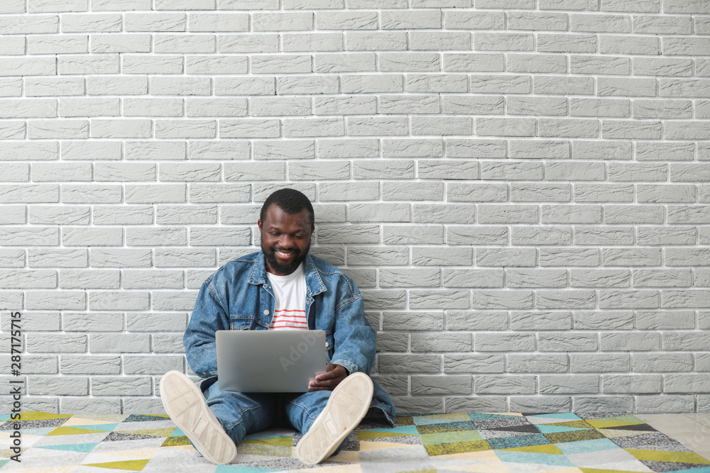 非裔美国博主拿着笔记本电脑坐在砖墙附近