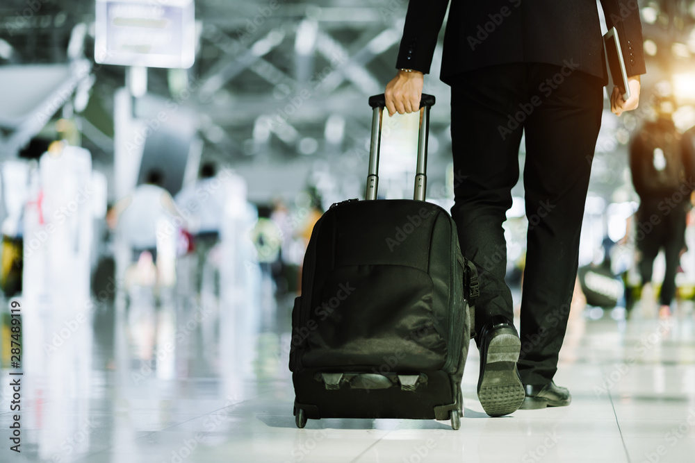 优雅的亚洲商人提着行李箱在机场内行走，用手机查看电子邮件，
